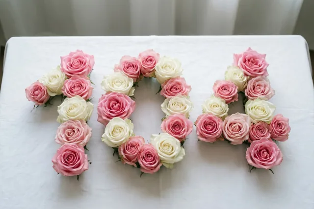 Roze en witte rozen vormen 104 op een wit tafelkleed, van bovenaf gefotografeerd in zacht licht.