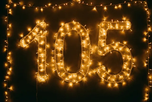 Warme lichtslingers vormen 105 tegen een donkere muur, omkaderd door een rand van soortgelijke goudkleurige lichtjes.