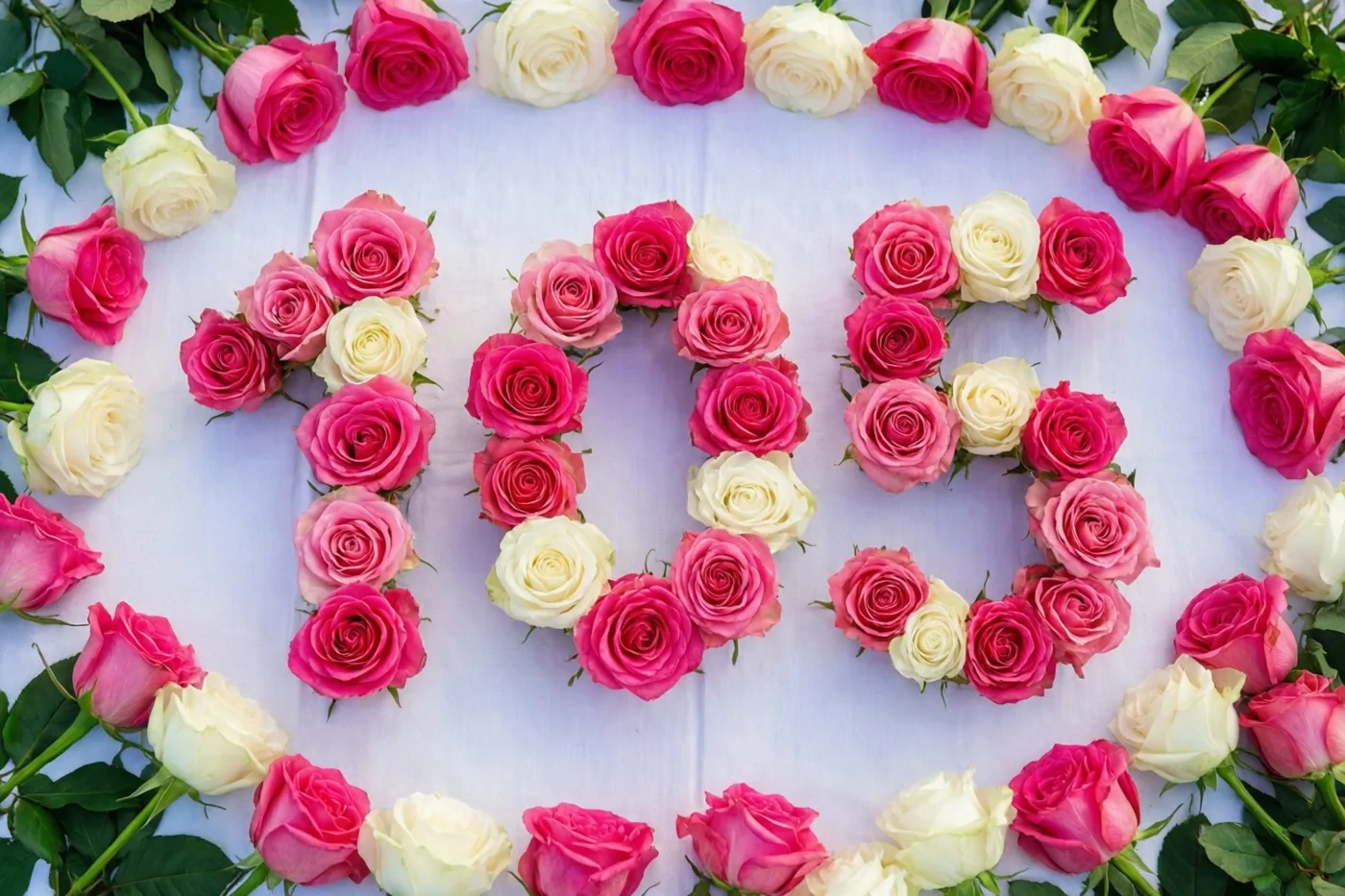 Van bovenaf zijn roze en witte rozen te zien die 105 vormen op een wit tafelkleed.
