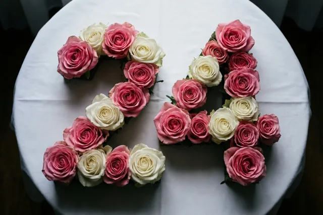 Roze en witte rozen vormen 24 op een wit tafelkleed, recht van boven gefotografeerd in zacht licht.