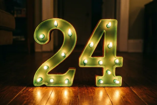 Brandende theelichtjes vormen 24 op een donkere houten vloer in een zacht verlichte binnenruimte.