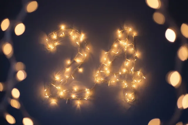 Warme lichtslingers vormen 24 tegen een donkere muur, met onscherpe feestlichtjes op de achtergrond.