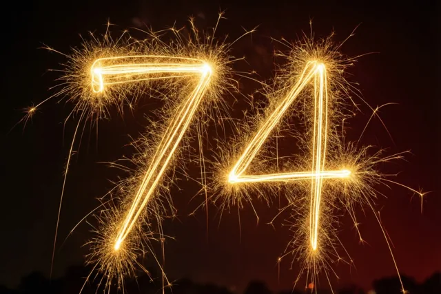 Het getal 74 is gevormd door gouden lichtsporen van sterretjes tegen een donkere nachthemel, met warme goudgele en oranje tinten.