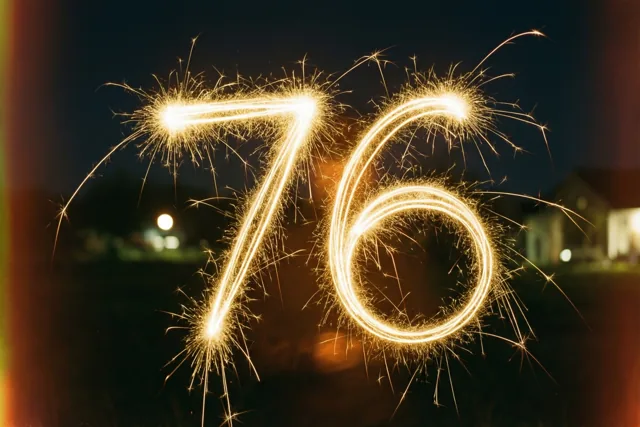 Gouden lichtsporen van sterretjes vormen 76 tegen een donkere nachthemel, met onscherpe lichtjes in de verte.