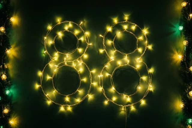 Warme lichtjes vormen 88 tegen een donkere muur, met groene slingers aan de zijkanten en onscherpe lichtvlekken op de achtergrond.