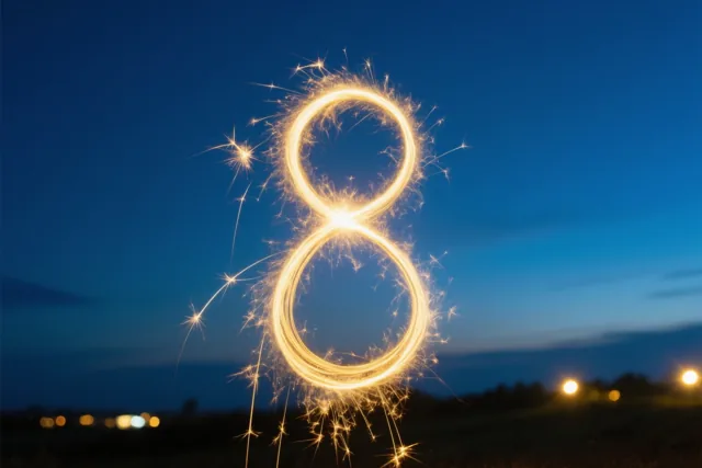 Gouden lichtsporen en vonken van sterretjes vormen een lichtgevende 8 tegen een diepblauwe avondhemel, met onscherpe lichtjes in de verte.