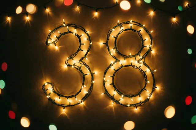 Het getal 38 is gevormd door warme lichtjes op een donkere muur, met onscherpe feestlichtjes op de achtergrond.