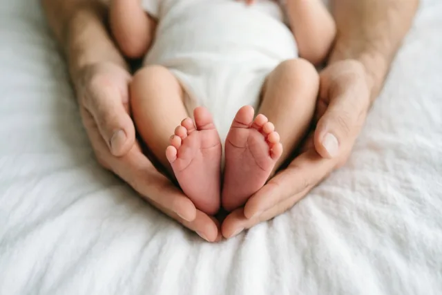 Een ouder houdt de voetjes van een pasgeboren baby vast op een witte deken, in zacht licht met warme huidtinten.