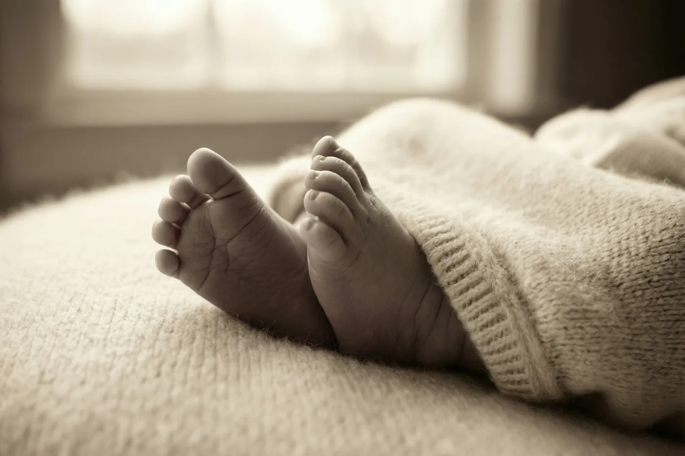 De kleine voetjes van een pasgeboren baby rusten op een lichte stof met structuur in zacht raamlicht.