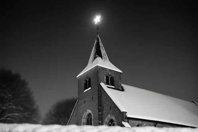Een zwart-witbeeld toont een besneeuwde Vlaamse kerk bij nacht met een heldere ster boven het dak en de toren.