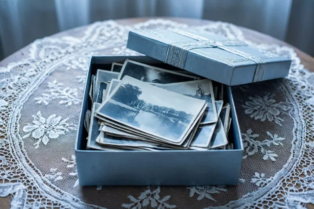 Een open blauwe fotodoos met oude zwart-witfoto's staat op een wit kanten tafelkleed in koele blauwe en witte tinten.