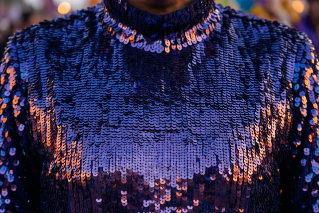 Een kostuum met overlappende blauwe pailletten is van dichtbij gefotografeerd en weerkaatst warm oranje en paars licht.