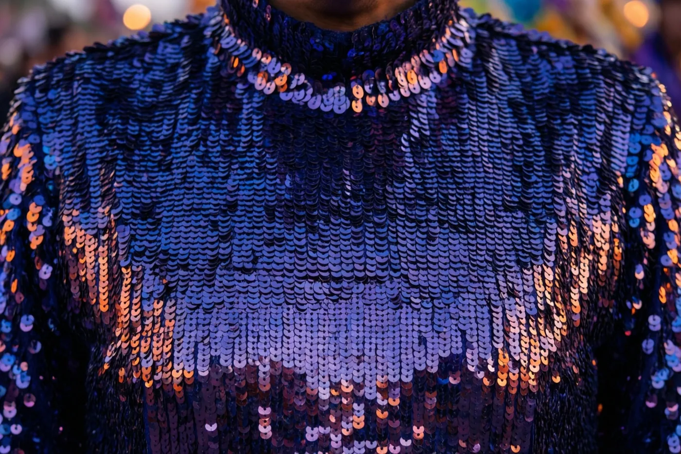 Een kostuum met overlappende blauwe pailletten is van dichtbij gefotografeerd en weerkaatst warm oranje en paars licht.