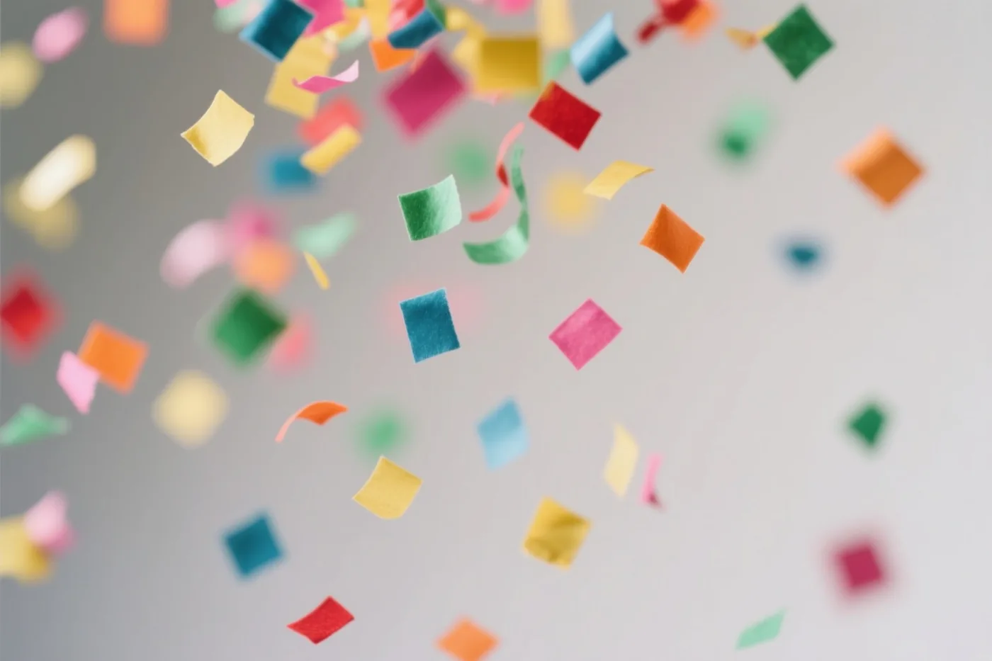 Kleurrijke vierkante en lintvormige stukjes confetti vallen door de lucht tegen een effen lichtgrijze achtergrond.