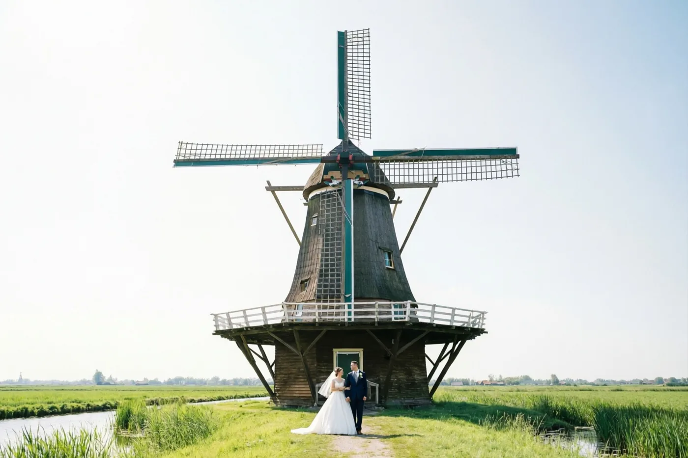 Een bruid en bruidegom staan voor een grote houten windmolen in een helder groen polderlandschap.