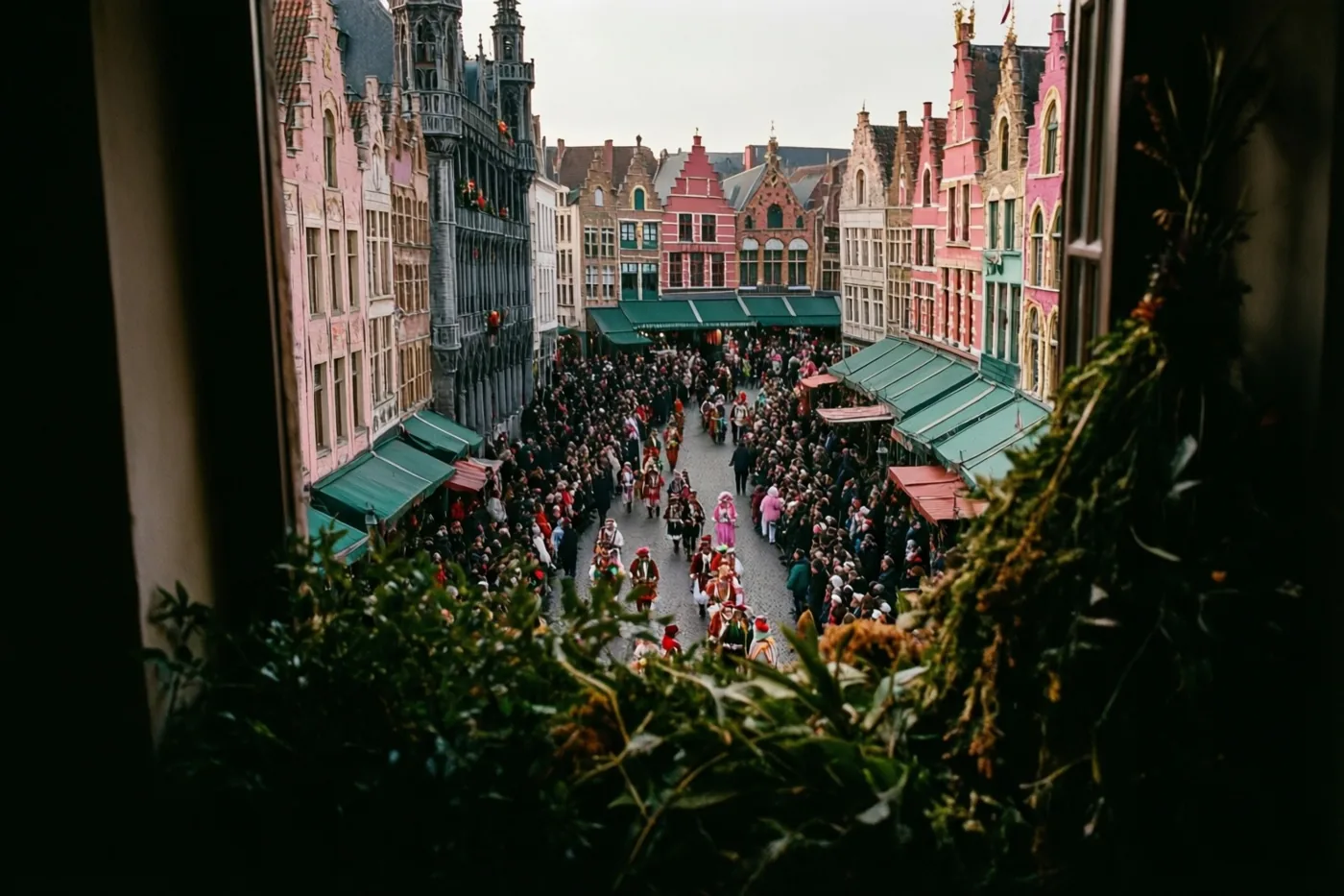 Door donkere raamkozijnen is van bovenaf een drukke carnavalsstoet op een Vlaams marktplein met kleurrijke historische gebouwen te zien, met groene bladeren op de voorgrond.