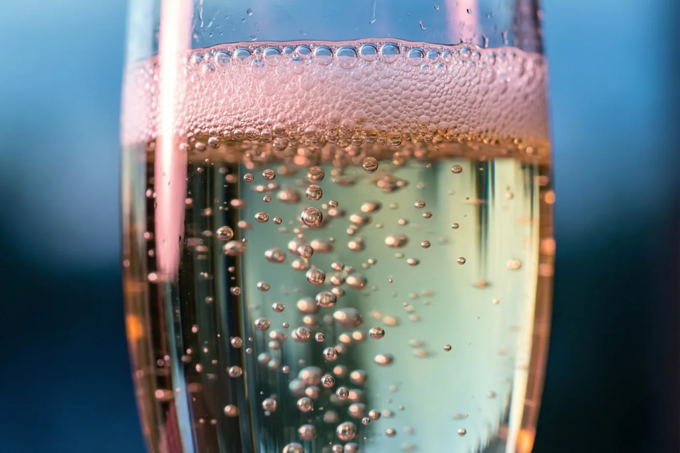 Fijne belletjes stijgen op in een hoog champagneglas tegen een wazige blauwe achtergrond.