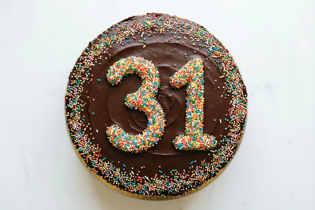 Een ronde chocoladetaart met 31 van gekleurde suikerstrooisels is van bovenaf gefotografeerd tegen een effen witte achtergrond.