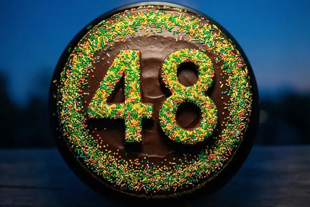 Een ronde chocoladetaart met 48 van gekleurde suikerstrooisels is recht van boven te zien tegen een donkerblauwe achtergrond.
