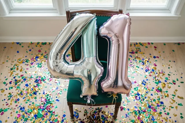 Zilveren en roségouden folieballonnen vormen 41 aan een groen gestoffeerde stoel in een lichte kamer met confetti op de houten vloer.