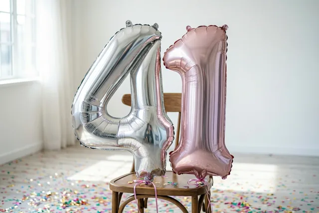 Twee grote folieballonnen vormen 41 aan een houten stoel in een lichte kamer met kleurrijke confetti en tinten van zilver, roségoud en wit.
