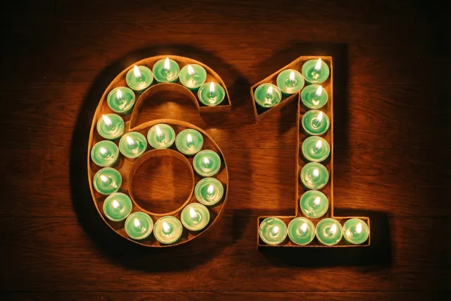 Groene theelichtjes staan brandend in de vorm van 61 op een donkere houten vloer.