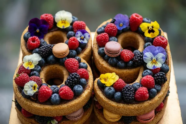 Een taart in de vorm van 89 is versierd met frambozen, blauwe bessen, bramen, eetbare bloemen en macarons, helder belicht tegen een onscherpe achtergrond.