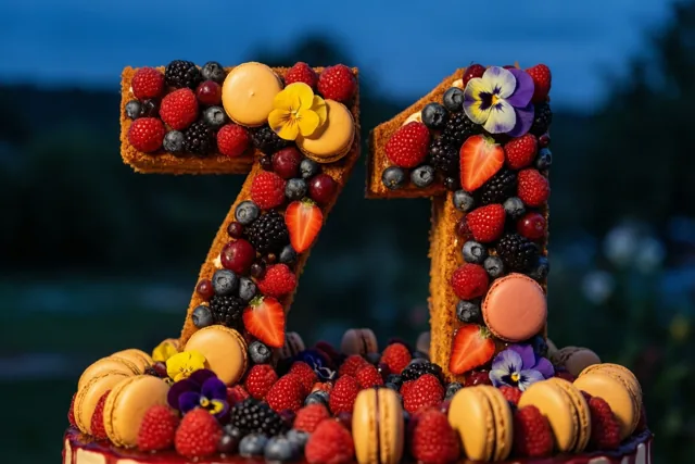 Een taart in de vorm van 71 met bessen, aardbeien, macarons en eetbare bloemen staat buiten in de schemering.
