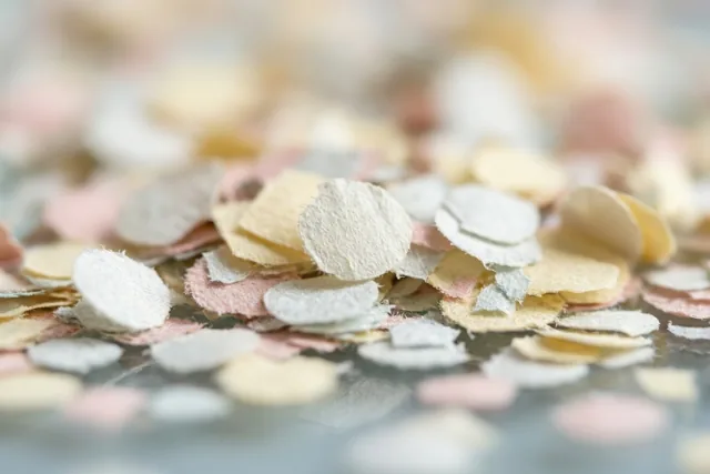 Roze, crèmekleurige en lichtgele confetti ligt verspreid over een glanzend oppervlak.