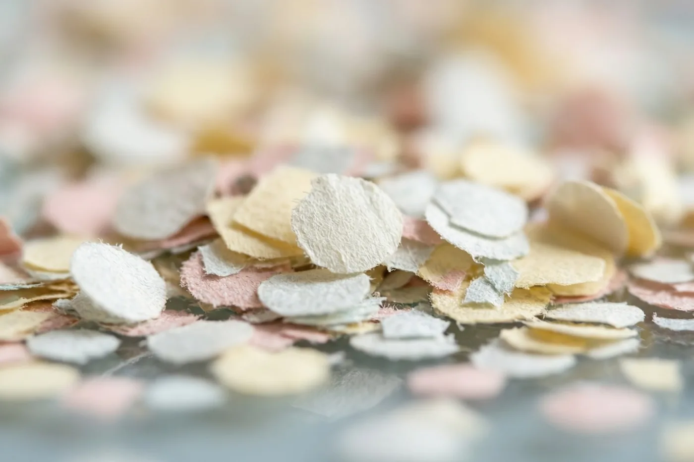 Roze, crèmekleurige en lichtgele confetti ligt verspreid over een glanzend oppervlak.