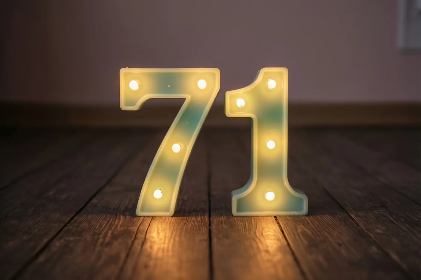 Brandende decoratieve lichtjes vormen het getal 71 op een donkere houten vloer binnenshuis.