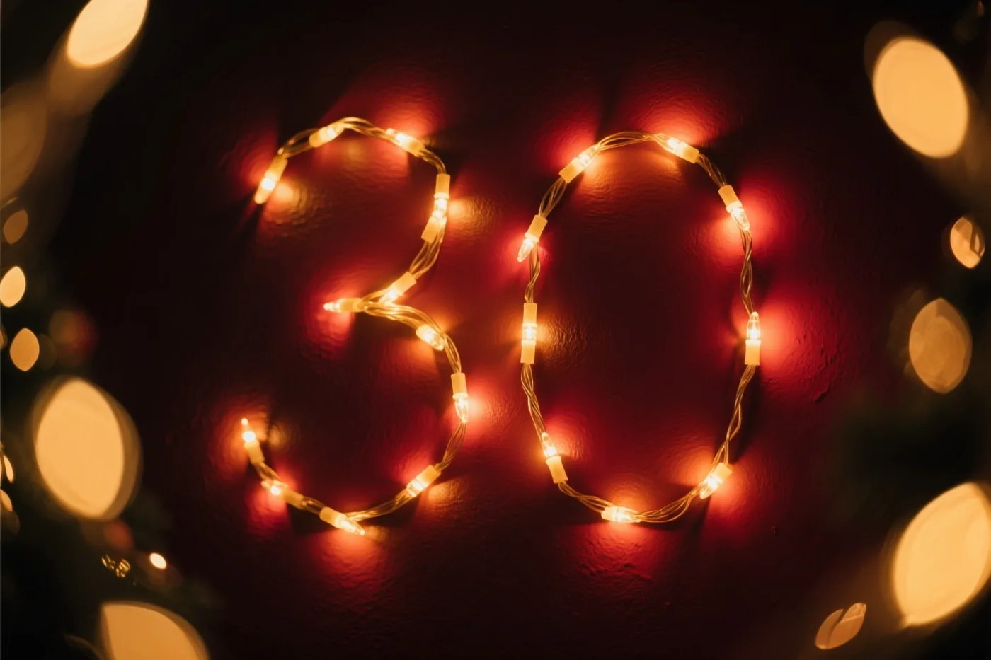 Warme lichtjes vormen het getal 30 op een donkerrode muur met structuur, met wazige lichtpunten op de achtergrond.