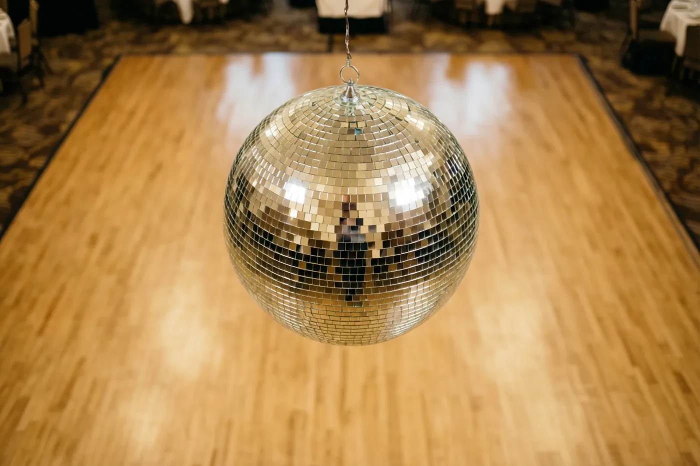 Een discobal hangt boven een glanzende houten dansvloer in een zwak verlichte zaal met warm licht.