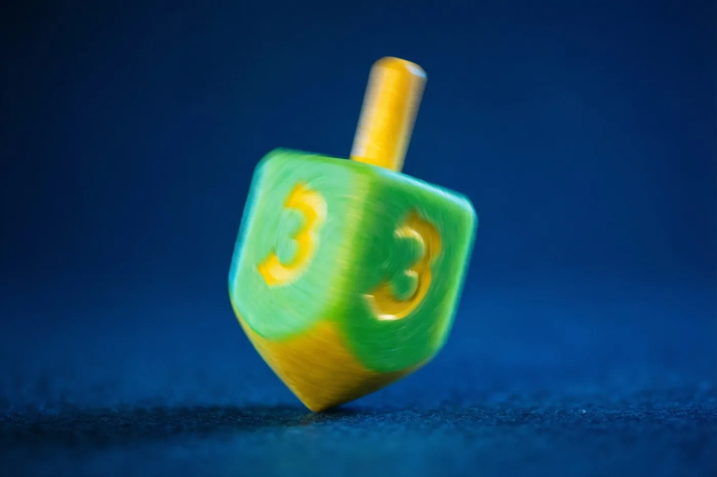 Een groene en gele dreidel draait snel tegen een diepblauwe achtergrond, met bewegingsonscherpte rond de tol.