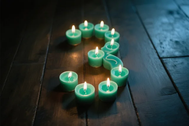 Brandende theelichtjes vormen het cijfer 3 op een donkere houten vloer, in een beeld met blauwgroene tinten.