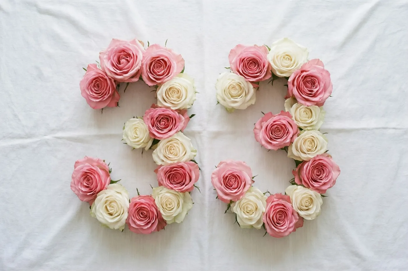Roze en witte rozen vormen het getal 33 op een wit tafelkleed, van bovenaf gezien.