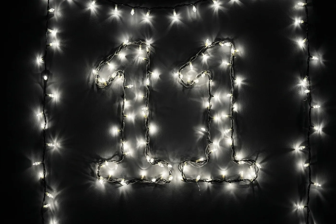 Warmwitte lichtjes vormen 11 op een donkere muur, met onscherpe lichtvlekken in beeld.