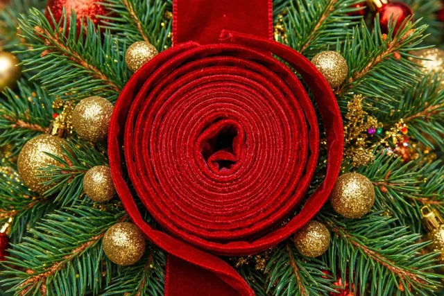 Een rood fluwelen lint ligt in een spiraal tussen groene dennennaalden en kerstballen met gouden glitter.