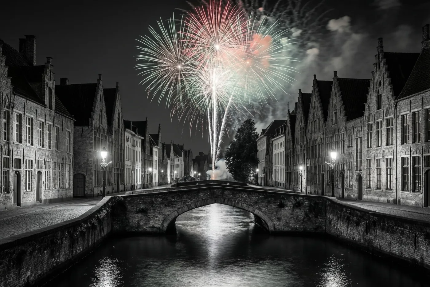 Een zwart-witbeeld toont een stenen brug over een vaart in een oud Vlaams stadje, met gekleurd vuurwerk erboven, straatverlichting en weerspiegelingen op het water.