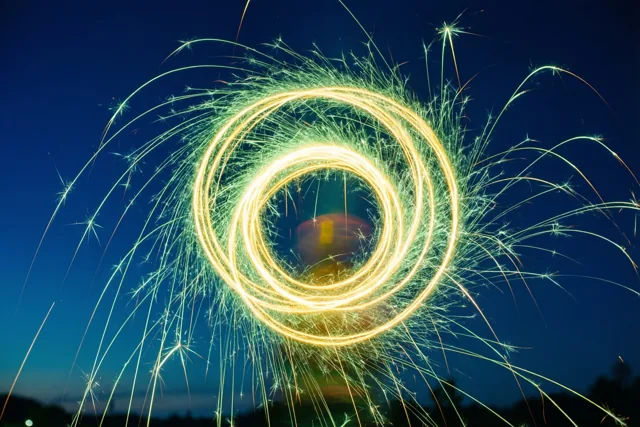 Felgele en groene lichtsporen van sterretjes vormen cirkels tegen een diepblauwe nachthemel.