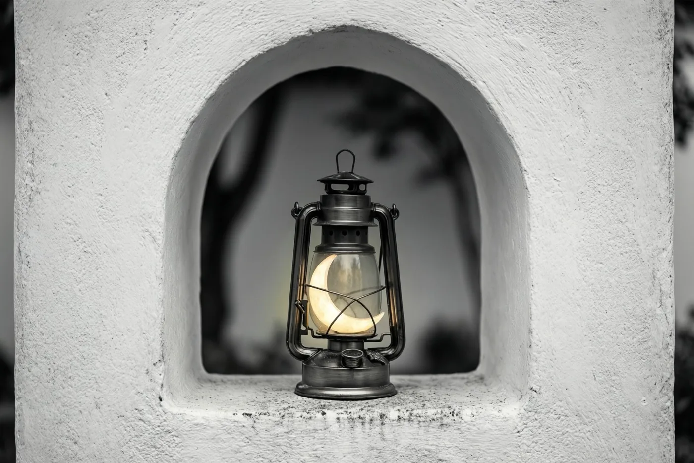 Een lantaarn in de vorm van een maansikkel straalt warm geel licht uit in een boogvormige nis van een witte pleistermuur, in een verder monochroom beeld.