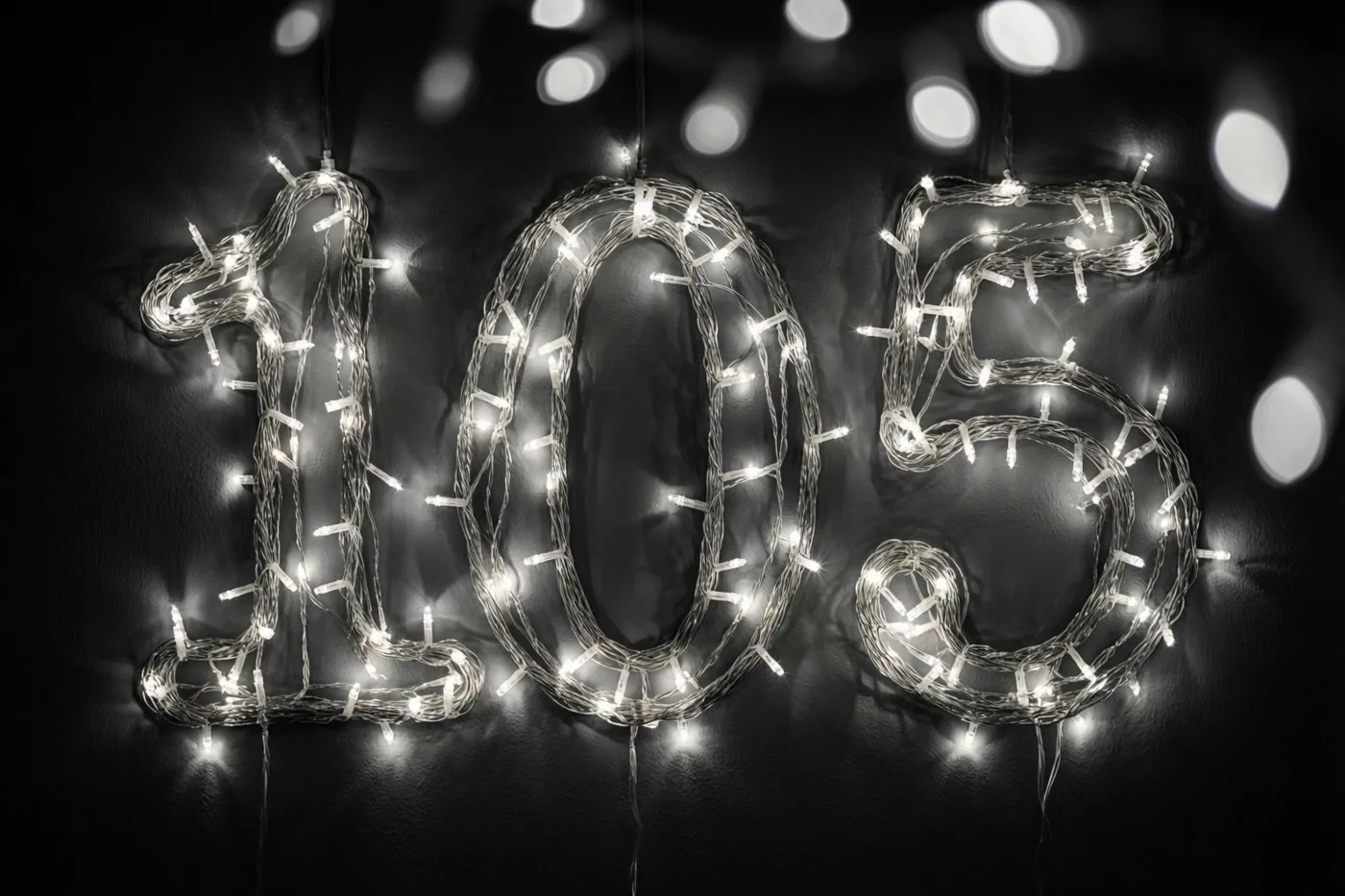 Lichtslingers vormen een gloeiende 105 tegen een donkere muur, met onscherpe lichtjes op de achtergrond.