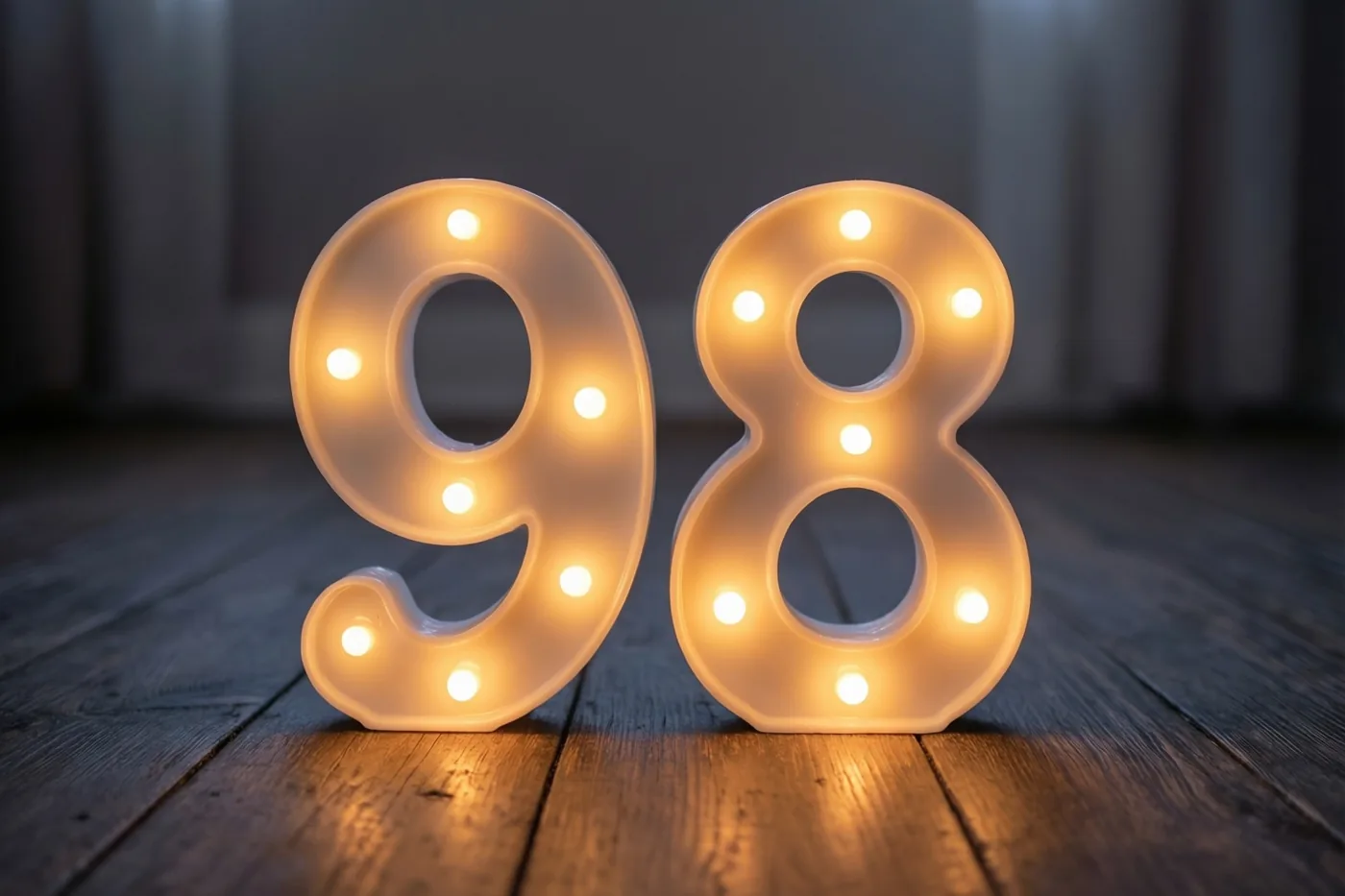 Warm gloeiende lampjes vormen het getal 98 op een donkere houten vloer.