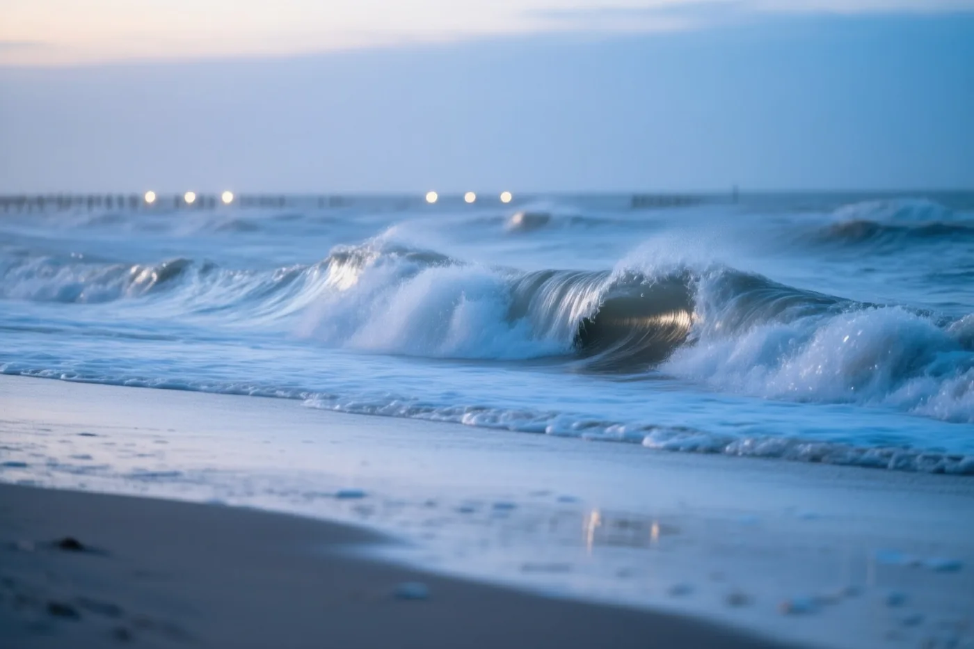 Hoge golven met schuimende toppen breken bij een leeg strand in blauwgrijs schemerlicht.