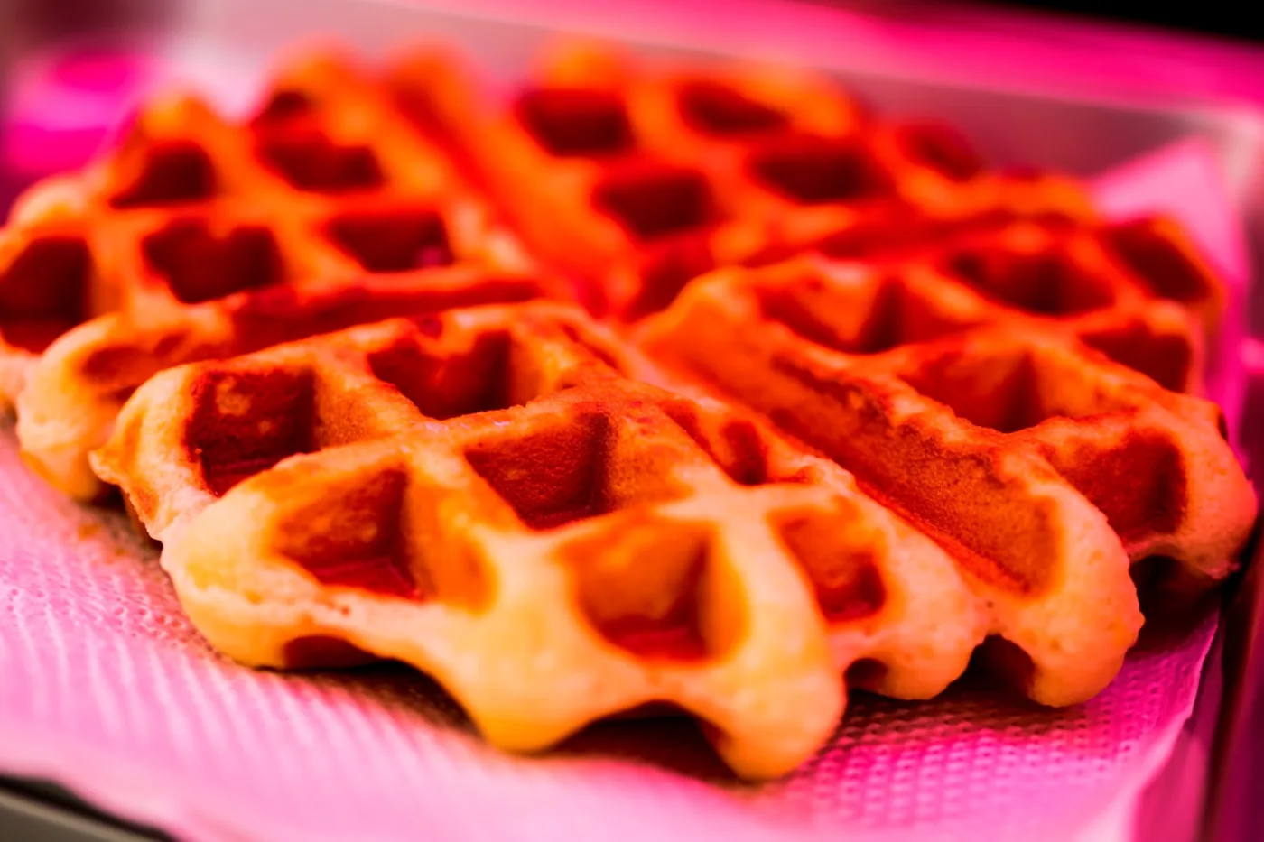 Goudbruine suikerwafels liggen op een roze servet met structuur in warm rozerood licht.