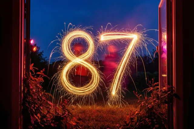 Gouden vonkensporen vormen 87 tegen een donkerblauwe nachtlucht, gezien door een open raam met een warme rode gloed eromheen.