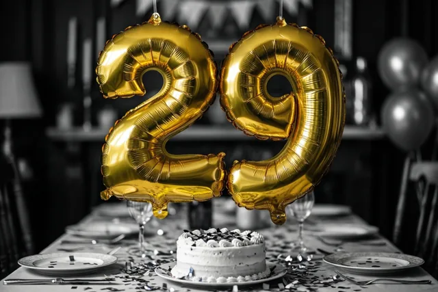 Gouden folieballonnen vormen het getal 29 boven een feesttafel met taart en confetti tegen een zwart-witte achtergrond.