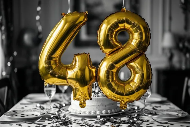 Grote gouden folieballonnen vormen 48 boven een feestelijk gedekte tafel met confetti en taart tegen een zwart-witte achtergrond.