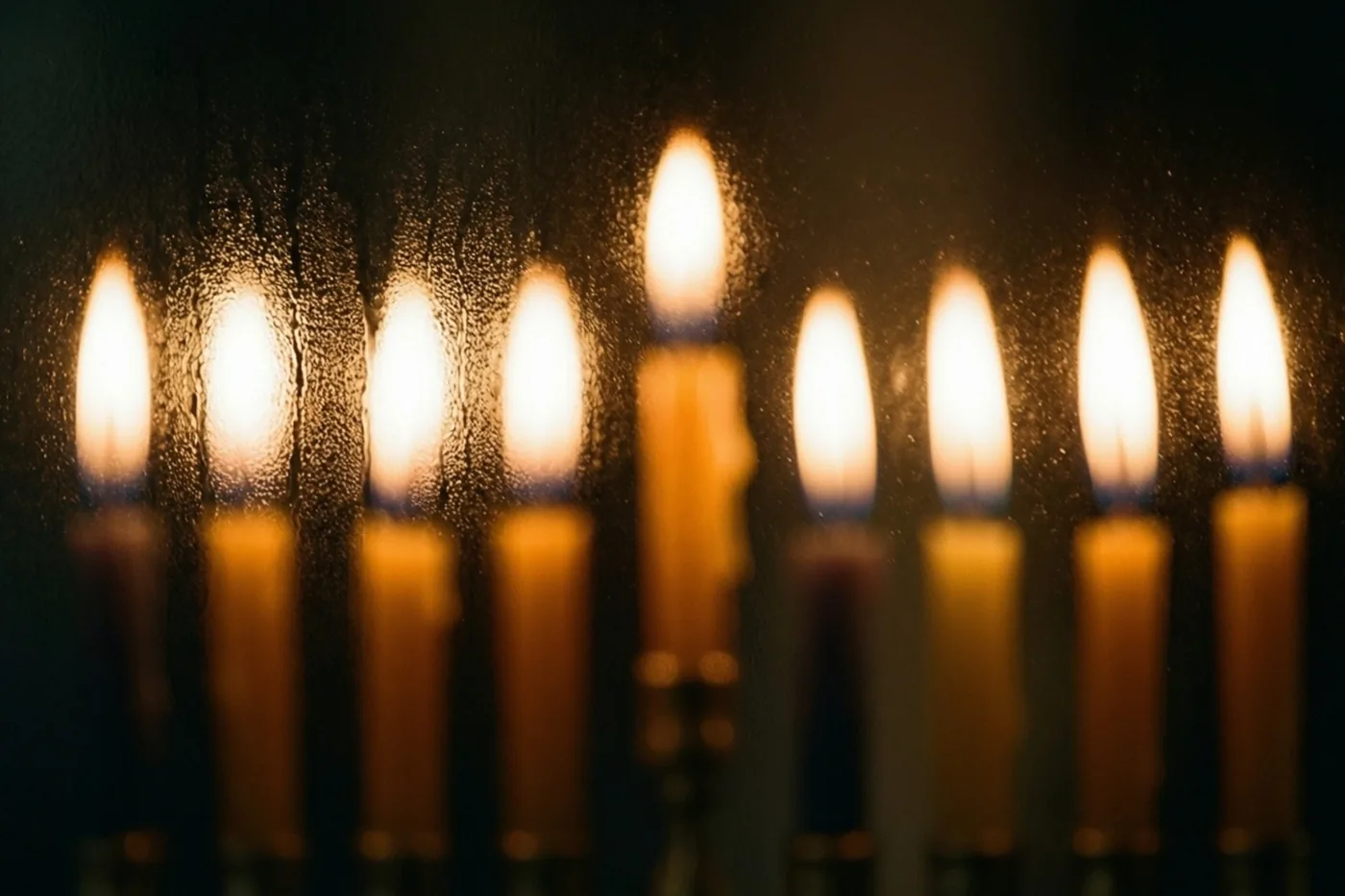 Een kandelaar met negen brandende kaarsen is door matglas te zien als zachte gouden en oranje lichtvlekken in het donker.