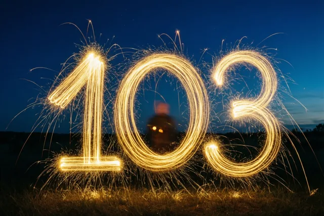 Gouden lichtsporen van sterretjes vormen 103 boven gras tegen een donkerblauwe nachthemel.